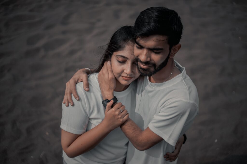 A loving couple embraces on a dark sandy beach, capturing a moment of intimacy and connection.